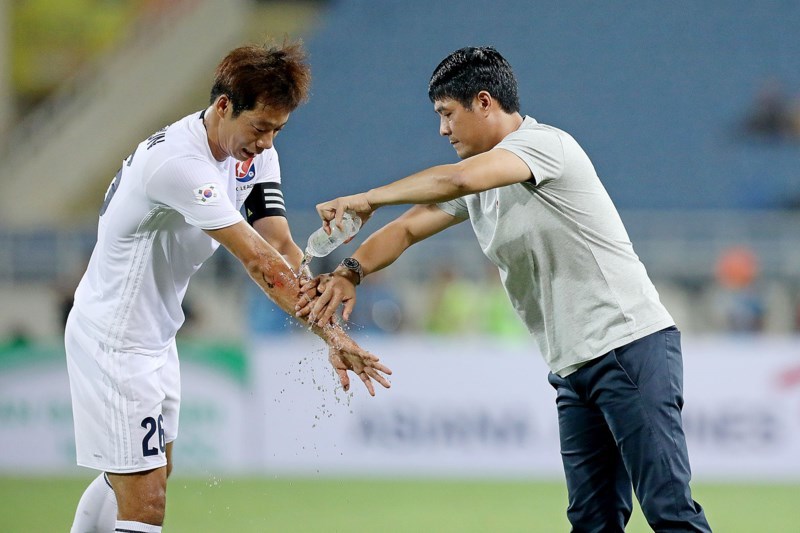 HLV Hữu Thắng rửa vết thương cho đội trưởng Yeom Ki Hun của đội Hàn Quốc. Ảnh: PLO