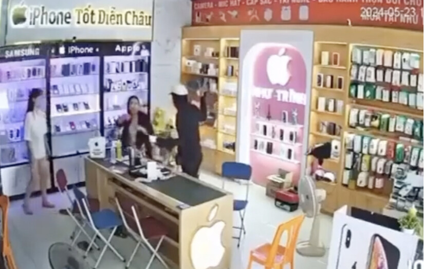 Đối tượng dùng súng giả và dao uy hiếp 2 cô gái trong cửa hàng điện thoại để cướp tài sản. Ảnh chụp từ video clip